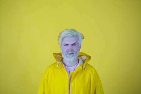 Portrait of a mature man with yellow hair in a yellow raincoat isolated on yellow background.の写真素材