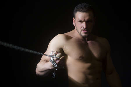 Muscular bodybuilder man training with chain at the gym.