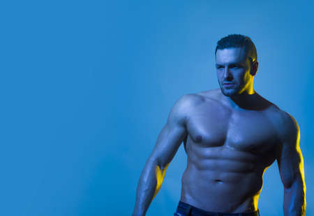 Portrait of a muscular man posing without a shirt against blue background.の写真素材