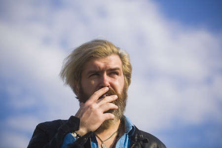 Fashion man smoking on sky background. Fashion smoker with cigarette on fresh air.の写真素材