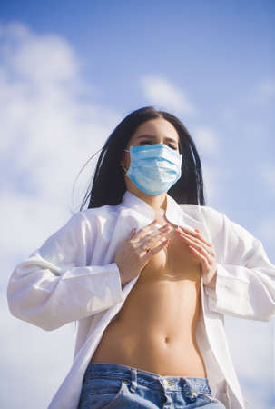 Young woman protecting herself from Corona virus covid 19 with a mask on blue sky background.の写真素材