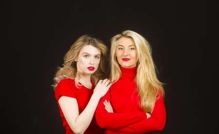 Friends forever. Two cute lovely girl friends in red posing with smile on dark background.の写真素材