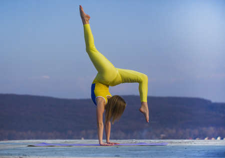 Beautiful athletic woman is stretching and makes a bridge on sky background.の写真素材