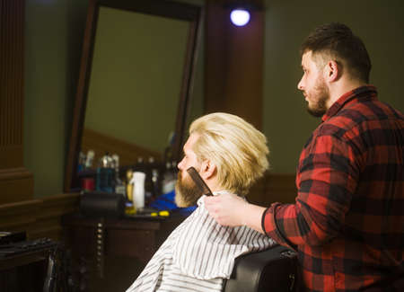 Professional barber styling hair of his brutal bearded client.の写真素材