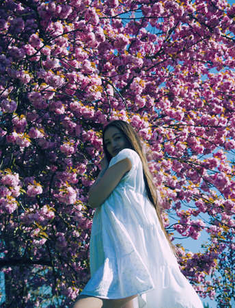 Portrait of young beautiful woman posing among blooming sakura trees.