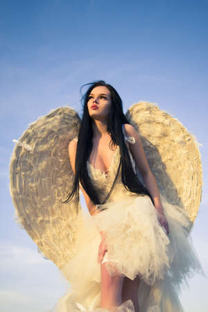 Sensual female angel posing over a cloudy sky with feathers.の写真素材