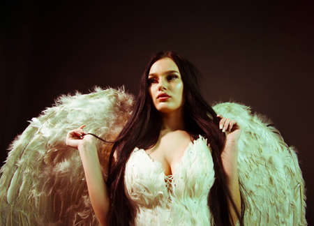 Beautiful brunette girl with white wings on black background.の写真素材