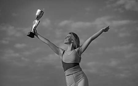 Young blonde sportswoman looking on champion Cup and posing with sky background. She is wearing yellow top and leggins.の写真素材