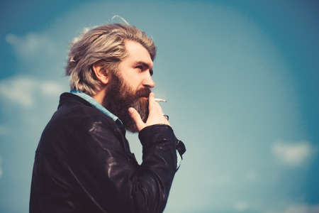 Face of a middle aged man smoking a cigarette and looking thoughtful. Set against a blue sky.の写真素材