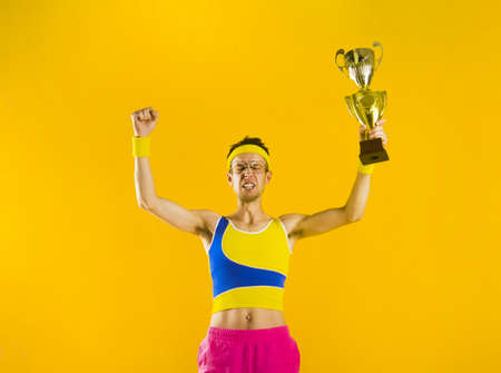 Funny man celebrate after winning gold cup isolated on yellow.