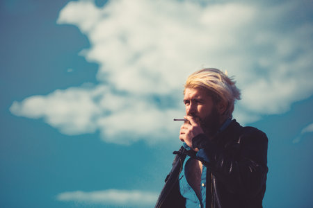 Cool mediterranean man with beard smoking outside in urban environment.の写真素材