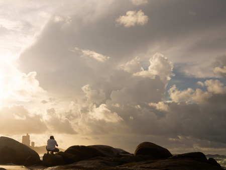 Male tourists Sitting down on the rocks to take pictures of the beautiful atmosphere of the sea in the morningの写真素材