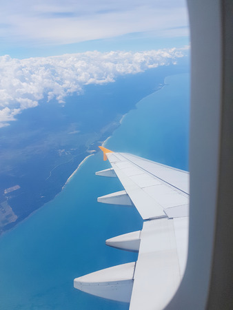 The wings of the plane on a cloud background and the bright sky. To shoot through a plane windowの写真素材