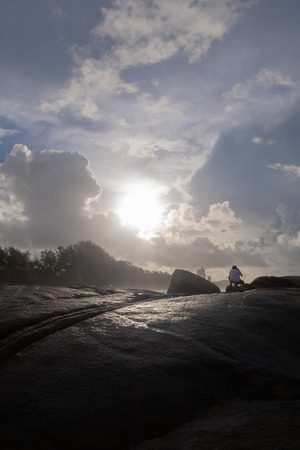 Large stone surface And the beautiful scenery of the sea and the sun light and clouds in the sky There is a photographer sitting to take pictures.の写真素材
