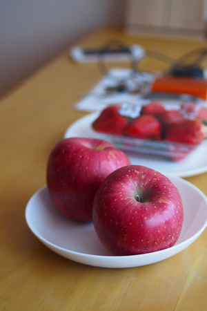 Red apples in a white plate are placed on a brown wooden table.の写真素材