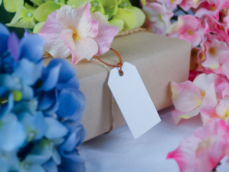 Brown gift box with blank paper labels and placed in the midst of blue and pink flowersの写真素材