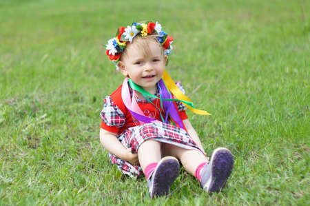 A little girl with a wreath on his head sitting in the grass              の写真素材