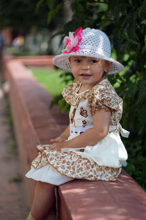 Two-year-old girl in a smart dress and hat sitting on the street                               の写真素材