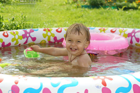 Two-year-old girl bathes in inflatable paddling pool and laughs          の写真素材