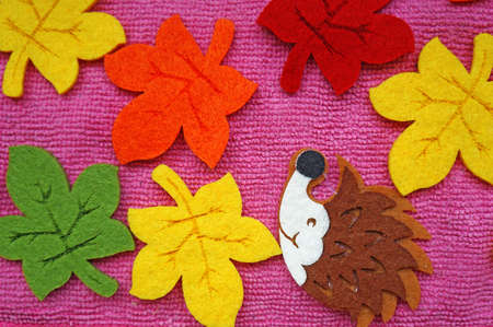 Hedgehog and colorful Maple leaves out of felt on a pink fabric as a backgroundの写真素材
