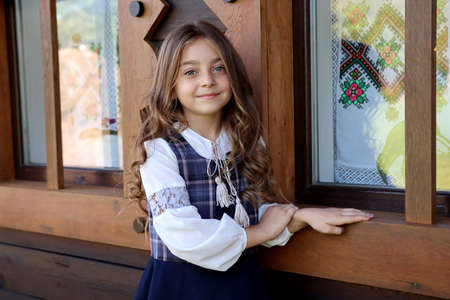 Cute little girl sits by the window of the house