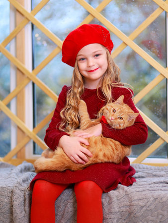 Blonde Little Girl in Red Admiring Her Cat by the Christmas Adorned Treeの写真素材
