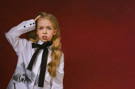 Portrait of a little girl in a white shirt and black tie on a red backgroundの写真素材