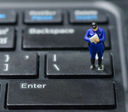 miniature policeman standing on the keyboard, computer security conceptの写真素材