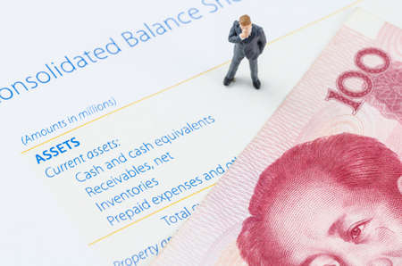 miniature businessman standing with Chinese banknote on the balance sheetの写真素材