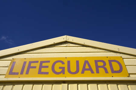 Yellow lifeguard sign, on yellow lifeguard hut, isolated against a blue sky.の写真素材