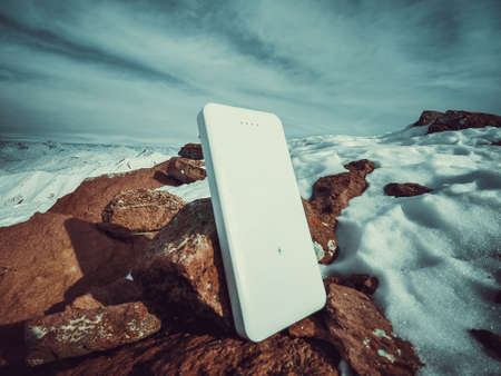 Power bank in hands. Tourist charges a devices in nature, against the backdrop of a winter mountains landscapeの写真素材