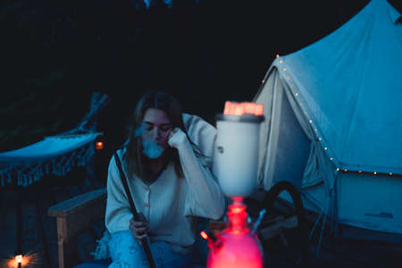 Girl smokes a hookah on the nature near the tent. Camping outdoor recreation.のeditorial素材