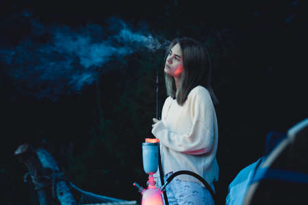 Girl smokes a hookah on the nature near the tent. Camping outdoor recreation.のeditorial素材