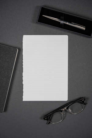 Pure white sheet of paper, notebook, glasses with a pen. Top view, space for textの写真素材