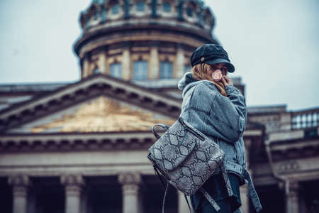 Traveler girl in warm clothes and a scarf turned to the camera on the background of Kazan Cathedral. Russia. Saint Petersburg.のeditorial素材