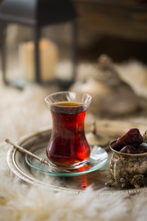 Tea set in oriental style in pear shaped glass with spoon and intage kettle and dates fruit on silver tray on sheep fur rugの写真素材