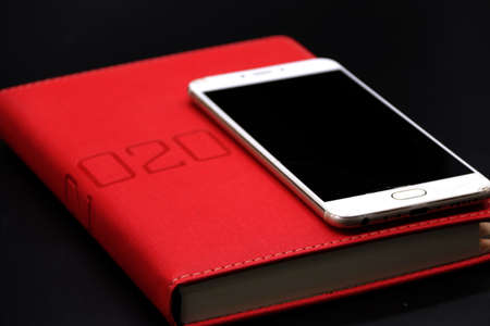 Black Screen Smartphone on the Red Notebook 2020, close up black background.の写真素材