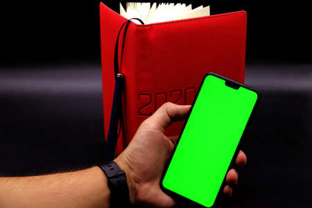 Chroma Key Man Holding Black Phone, Red Notebook 2020 , Black Background Mock up.の写真素材