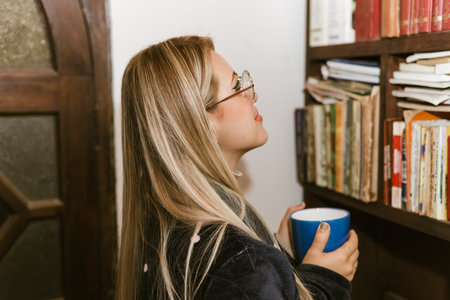 Book Day, April 23rd. Blonde woman with glasses reading a book while drinking chocolate.