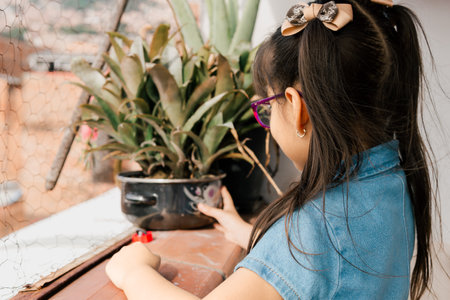 Beautiful Latina girl with pink glasses, looking at the plants on the balcony of her house. Children day, family day. Infant.の写真素材