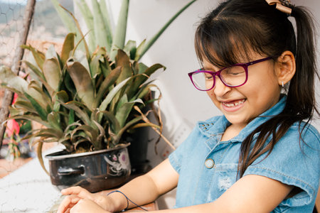 Beautiful Latina girl with pink glasses, smiling with her eyes closed on the balcony of her house. Children day, family day. Infantの写真素材
