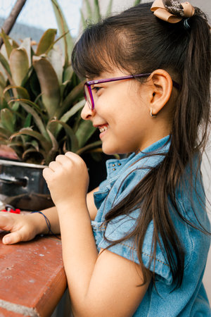 Beautiful Latina girl with pink glasses, smiling on the balcony of her house. Children day, family...