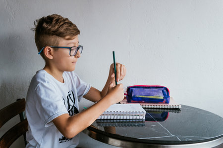 Latin boy with glasses drawing a picture in his notebook. Back to school, childhood. Homework and classes.の写真素材