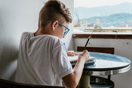 Latin boy with glasses drawing a picture in his notebook. Back to school, childhood. Homework and...