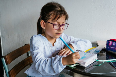 Latina girl in glasses doing chores at home. Coloring a notebook. Back to school. Childhood and painting.の写真素材