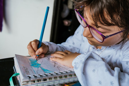 Latina girl in glasses doing chores at home. Coloring a notebook. Back to school. Childhood and...