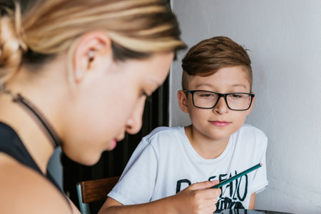 Latin boy with glasses, with his mother doing chores at home. Back to school. Childhood, notebooks and playful games.の写真素材