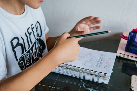 Latin boy with glasses drawing a picture in his notebook. Back to school, childhood. Homework and classes.の写真素材