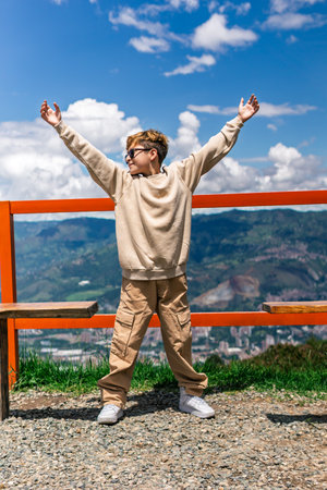 Latino boy enjoying nature with arms raised on a sunny mountain dayの写真素材