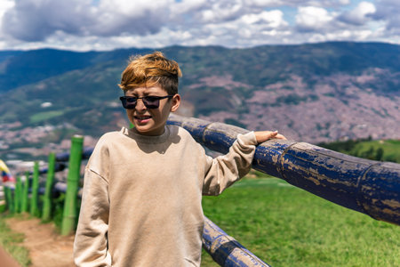 Colombian boy shielding his eyes from sunlight while standing by a scenic overlook above a mountain cityの写真素材